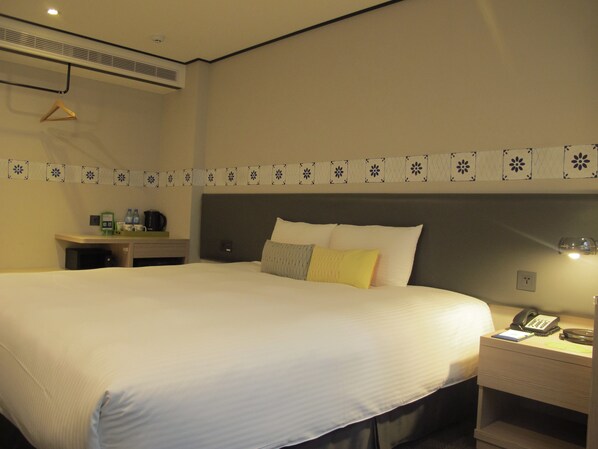 Una habitación de hotel con una cama grande, una mesita de noche con teléfono y una mesita con lámpara.
