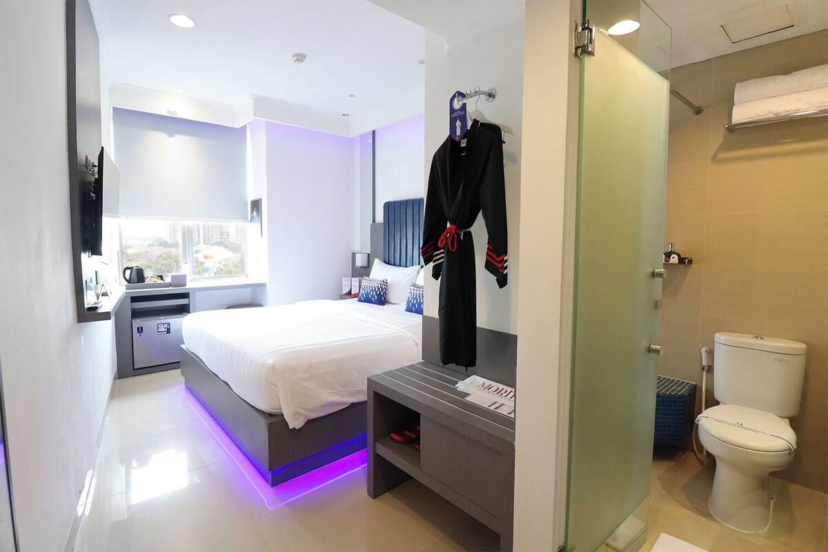 A modern hotel room with a bed, bedside table, and a bathroom with a toilet and shower.
