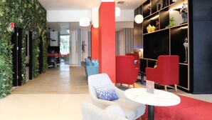 Un hall d’entrée moderne avec un mur d’accent rouge, un espace salon avec des canapés rouges et gris, et un mur végétal.