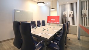 Une salle de conférence avec une longue table, des chaises noires, un tableau blanc et un écran rouge affichant le mot « MORITZ ».