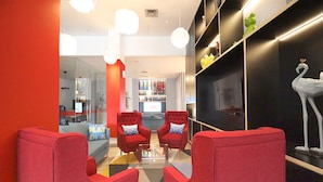 Un hall d’entrée moderne avec des fauteuils rouges, un mur noir orné d’une sculpture blanche et une cloison en verre donnant sur un espace de jeux.