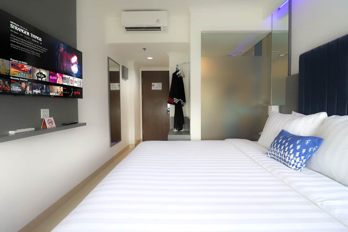 A hotel room with a large bed, a TV mounted on the wall displaying a movie poster, a coat rack, and a mirror.
