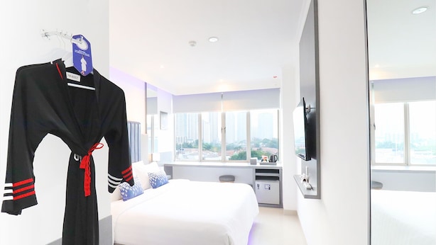 Une chambre d’hôtel avec un lit, une télévision, une fenêtre donnant sur la ville et un peignoir suspendu à un porte-manteau.