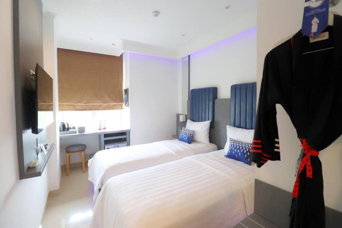 A hotel room with two beds, a desk, a chair, a TV, and a robe hanging on the wall.