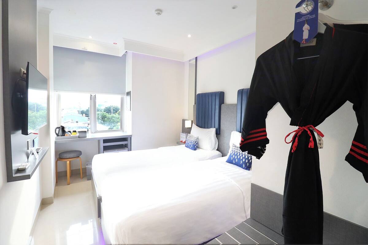 A hotel room with a large bed, a desk, a chair, a robe hanging on the wall, and a window with a view.