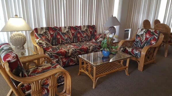 A living room with a floral sofa, two wicker chairs, a glass coffee table, and a lamp. - Ilikai Hotel by Hello Relaxation (Honolulu)
