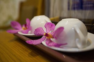 Un plateau avec deux tasses à thé blanches et des orchidées violettes.