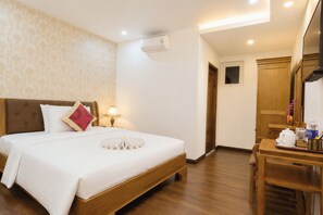 A hotel room with a bed, bedside table, lamp, wooden wardrobe, and a small window.