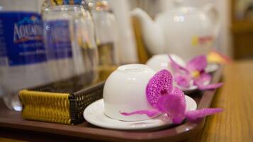 A tray with a white teapot, a white cup, and a purple orchid decoration.