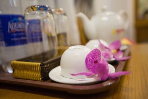 Un plateau avec une théière blanche, une tasse blanche et une décoration en forme d’orchidée violette.