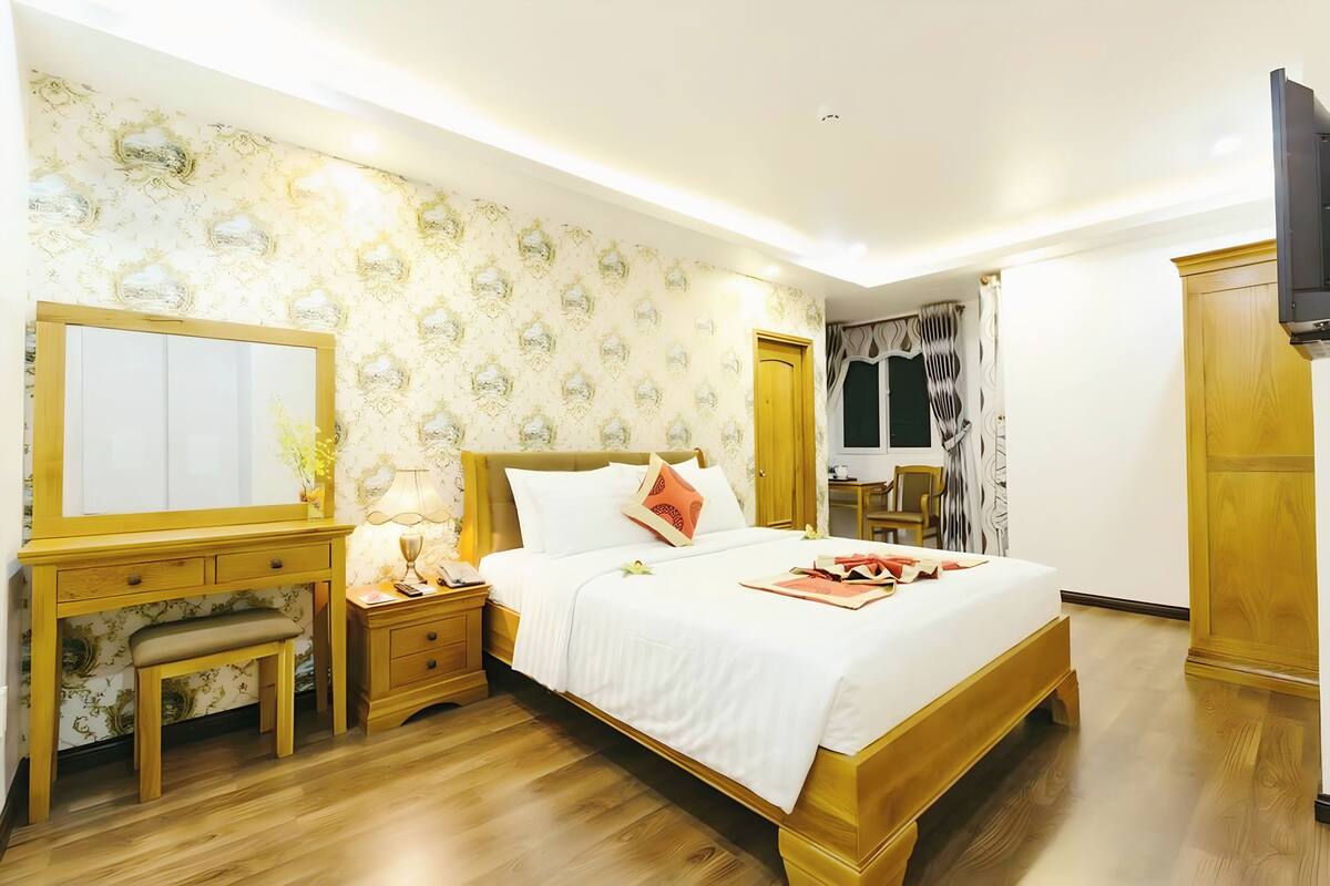 A bedroom with a wooden bed, a bedside table with a lamp, a mirror, and a wardrobe.
