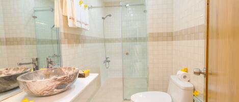 A bathroom with a glass-enclosed shower, a marble sink, and a toilet.