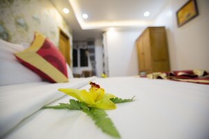 A hotel room with a bed, a flower on the bed, and a view of the hallway.