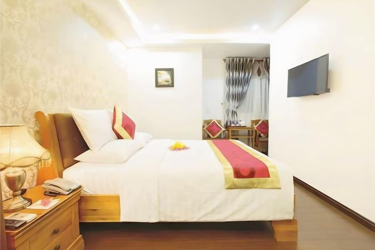 A hotel room with a bed, bedside table, lamp, and a TV mounted on the wall.