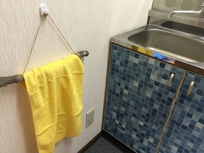 A bathroom with a yellow towel hanging on a towel rack, a sink with a blue tiled cabinet, and a wall socket. - Gerobal Hostel (Gero)