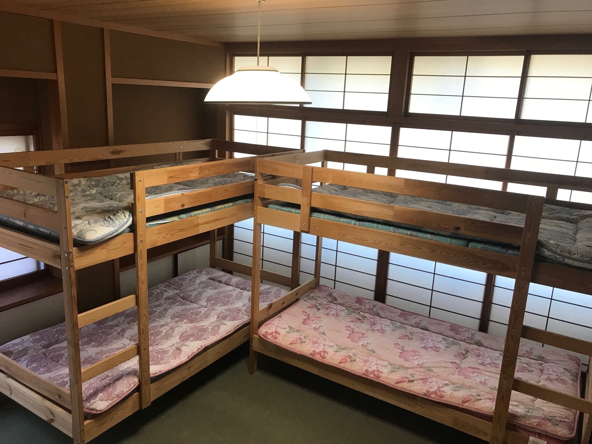 Ein Zimmer mit Etagenbetten, einer Hängelampe und einem Fenster mit Gittermuster.