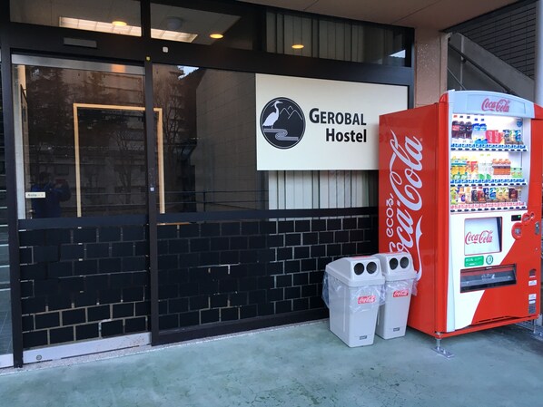 A hostel entrance with a Coca-Cola vending machine and trash bins. - Gerobal Hostel (Gero)