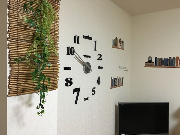 A wall clock with numbers and hands, a television, and a shelf with books and a clock.