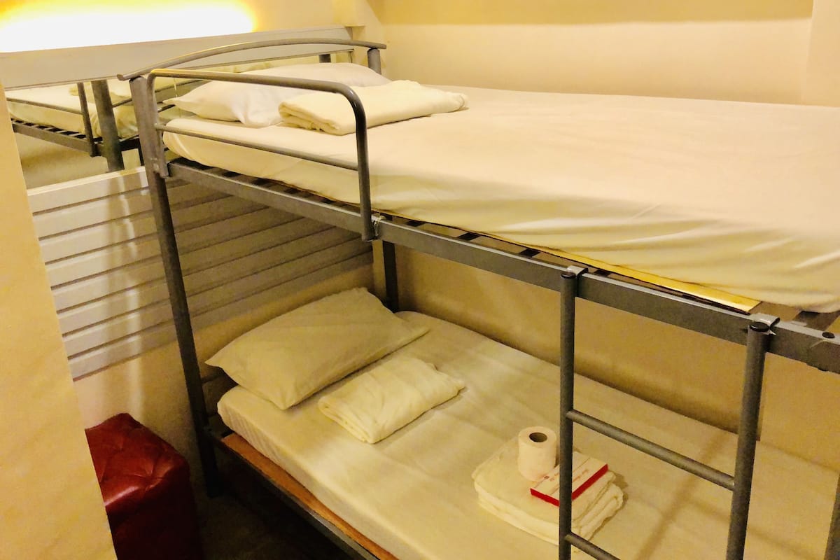 A bunk bed with white bedding and a red stool.