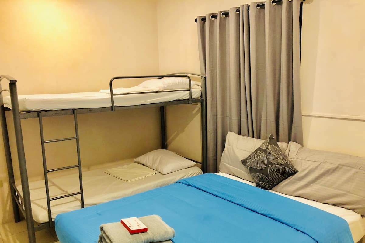 A bunk bed room with a blue bedspread, a white pillow, and a grey curtain.