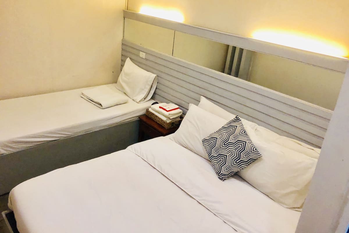 A small, single-bed room with a headboard, a bedside table with a lamp, and a mirror.