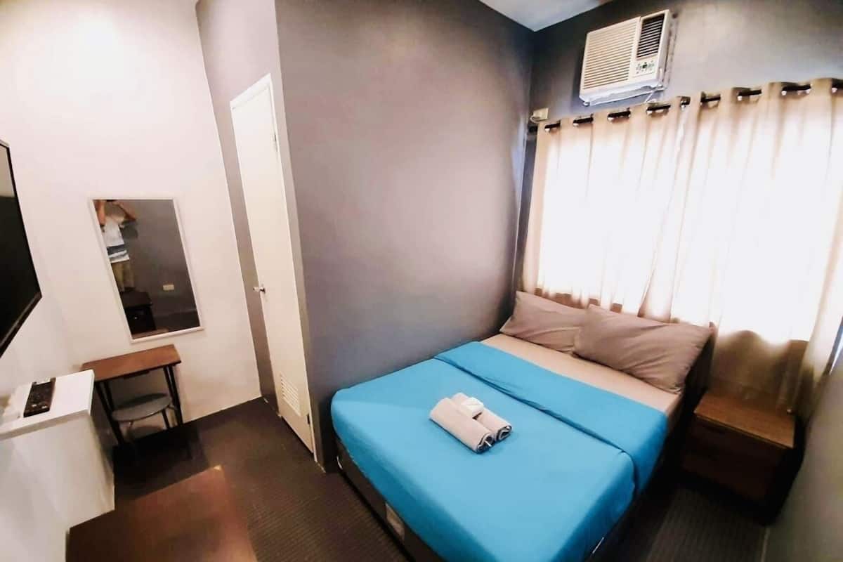 A hotel room with a bed, a desk, a chair, and a window with curtains.