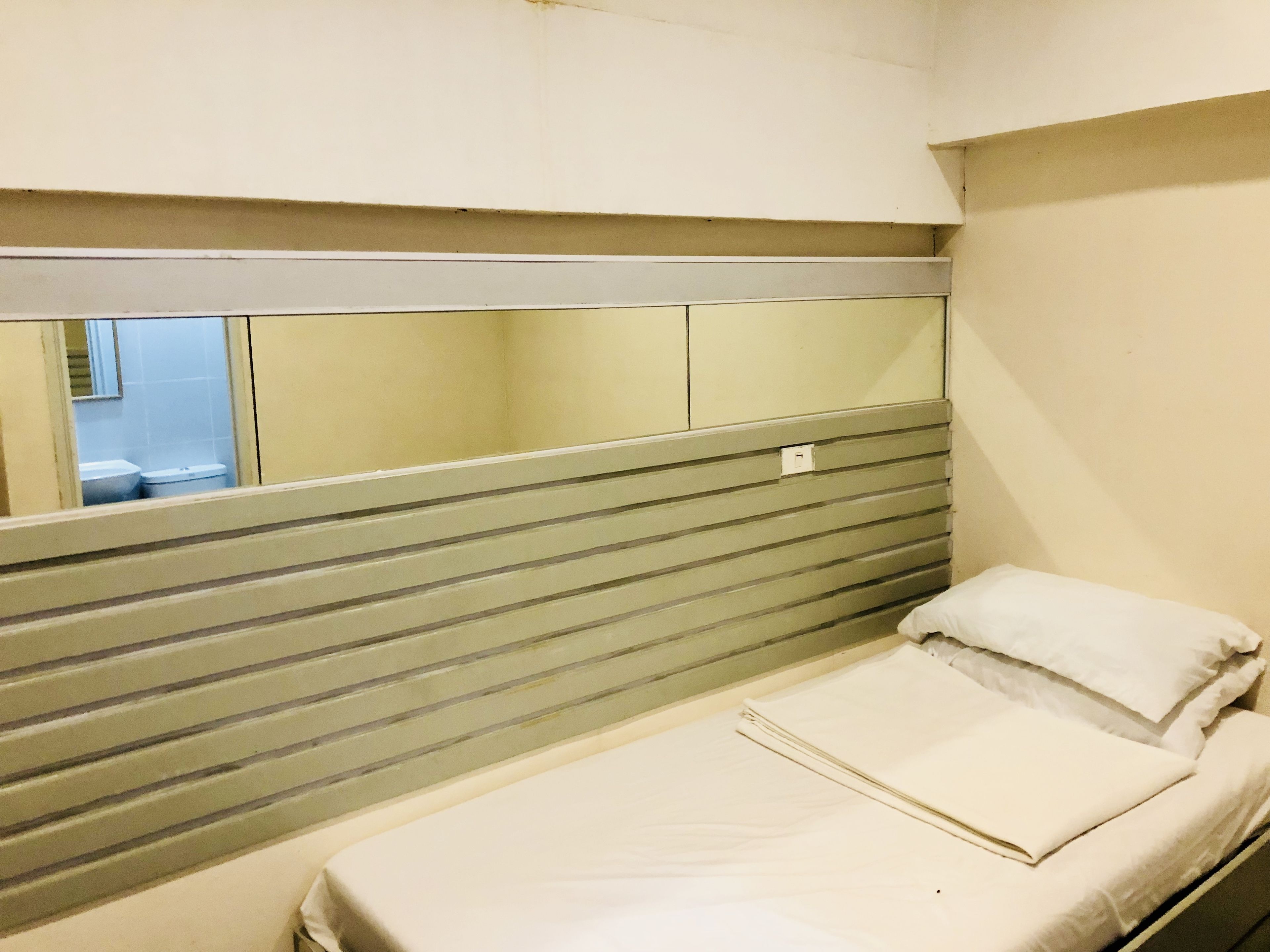 Una habitación pequeña con cama individual, cabecera a rayas, un espejo y una ventana.