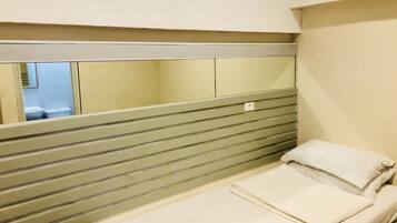 Una habitación pequeña con cama individual, cabecera a rayas, un espejo y una ventana.