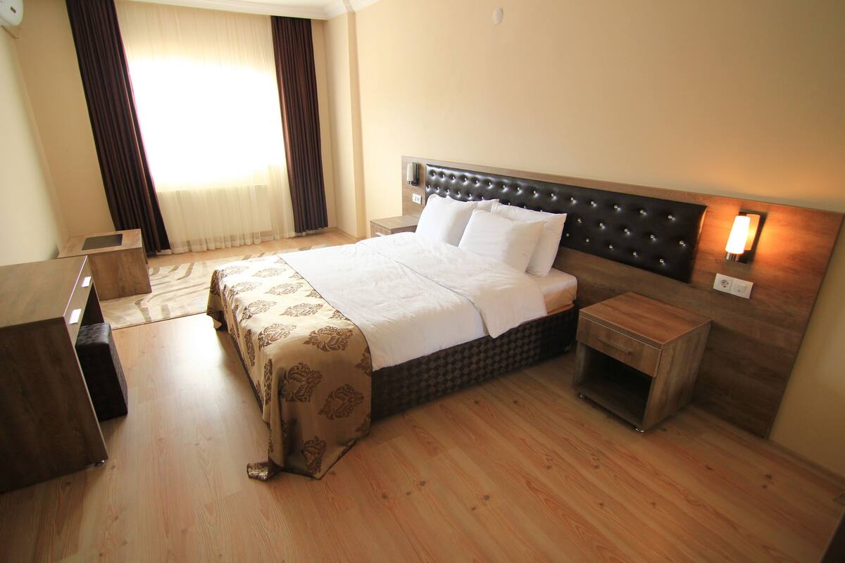 A hotel room with a large bed, a bedside table, a nightstand, and a window with curtains.