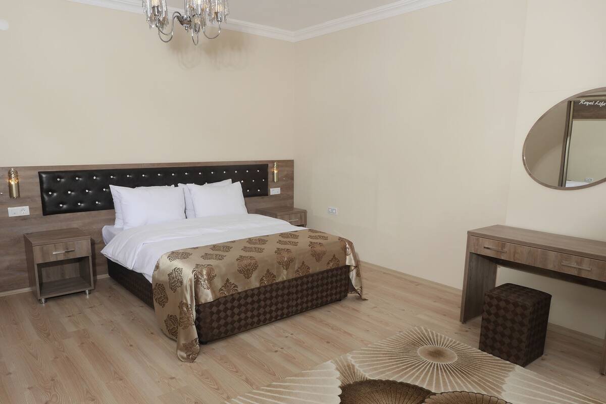 A hotel room with a bed, bedside tables, a dresser, a mirror, and a chandelier.