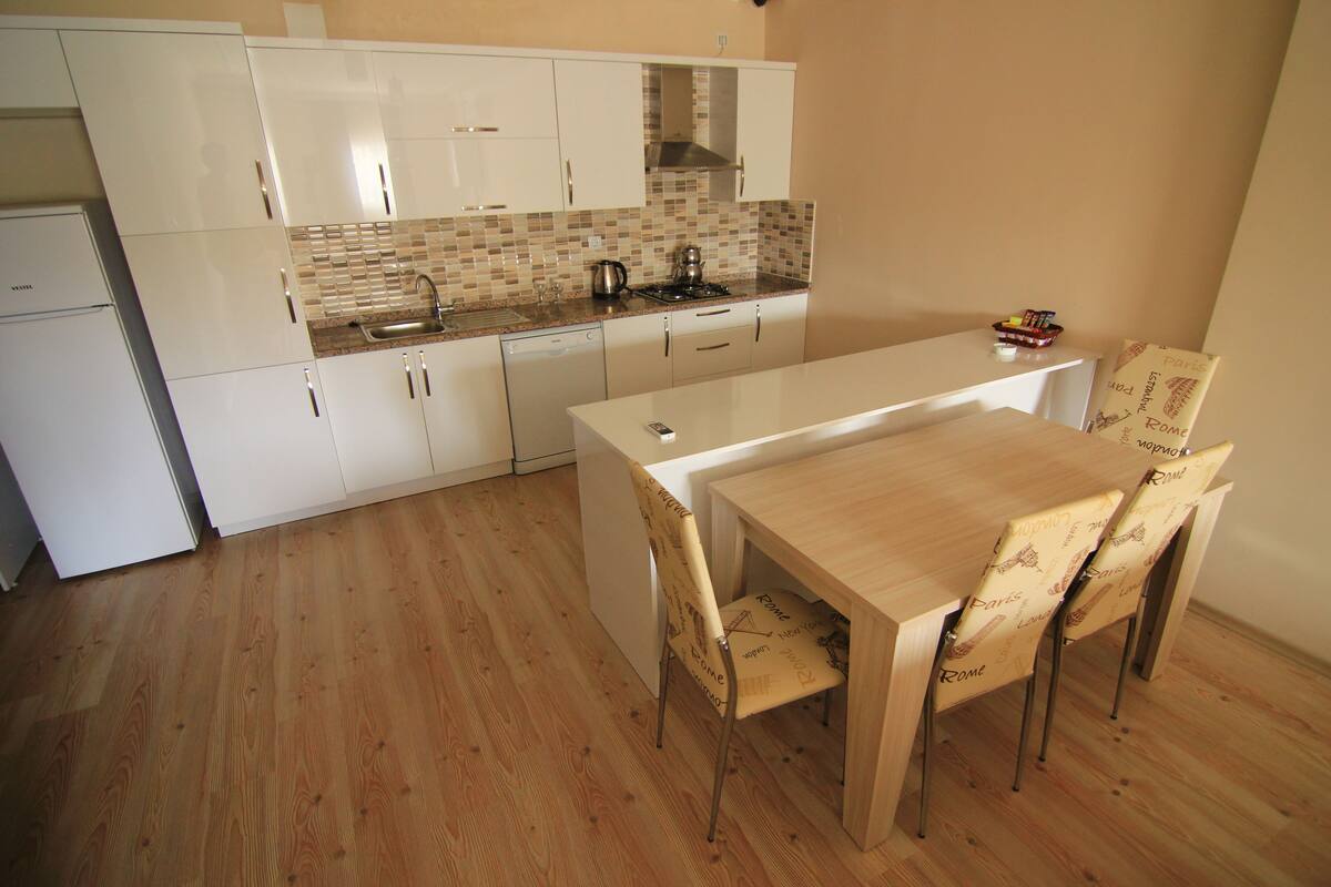 A compact kitchen with white cabinets, a tiled backsplash, and a wooden dining table with matching chairs.