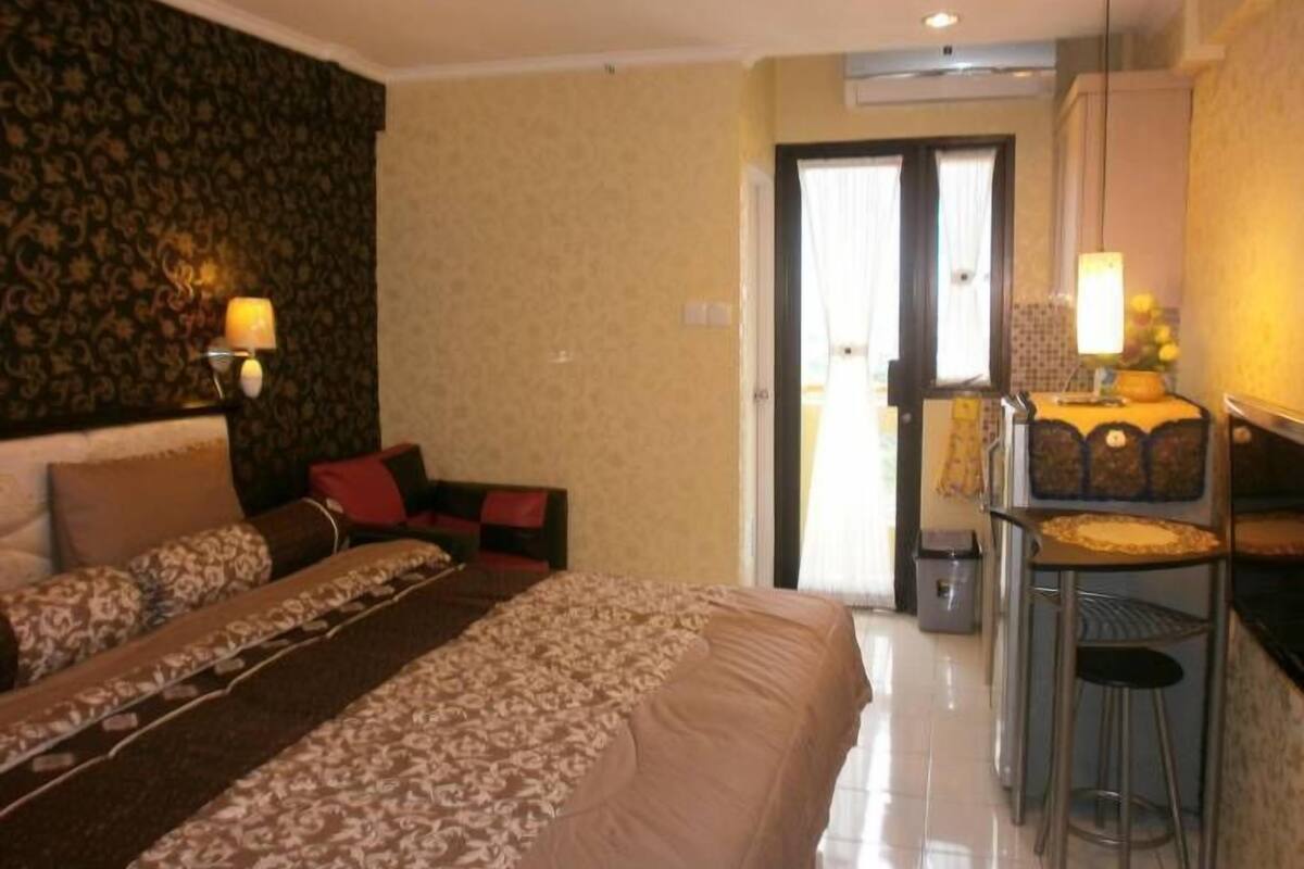 Une chambre d’hôtel avec un grand lit, un bureau avec une chaise, une petite table avec une lampe et une porte donnant sur un balcon.
