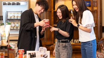 A group of people in a room with a table displaying food items and a refrigerator in the background.