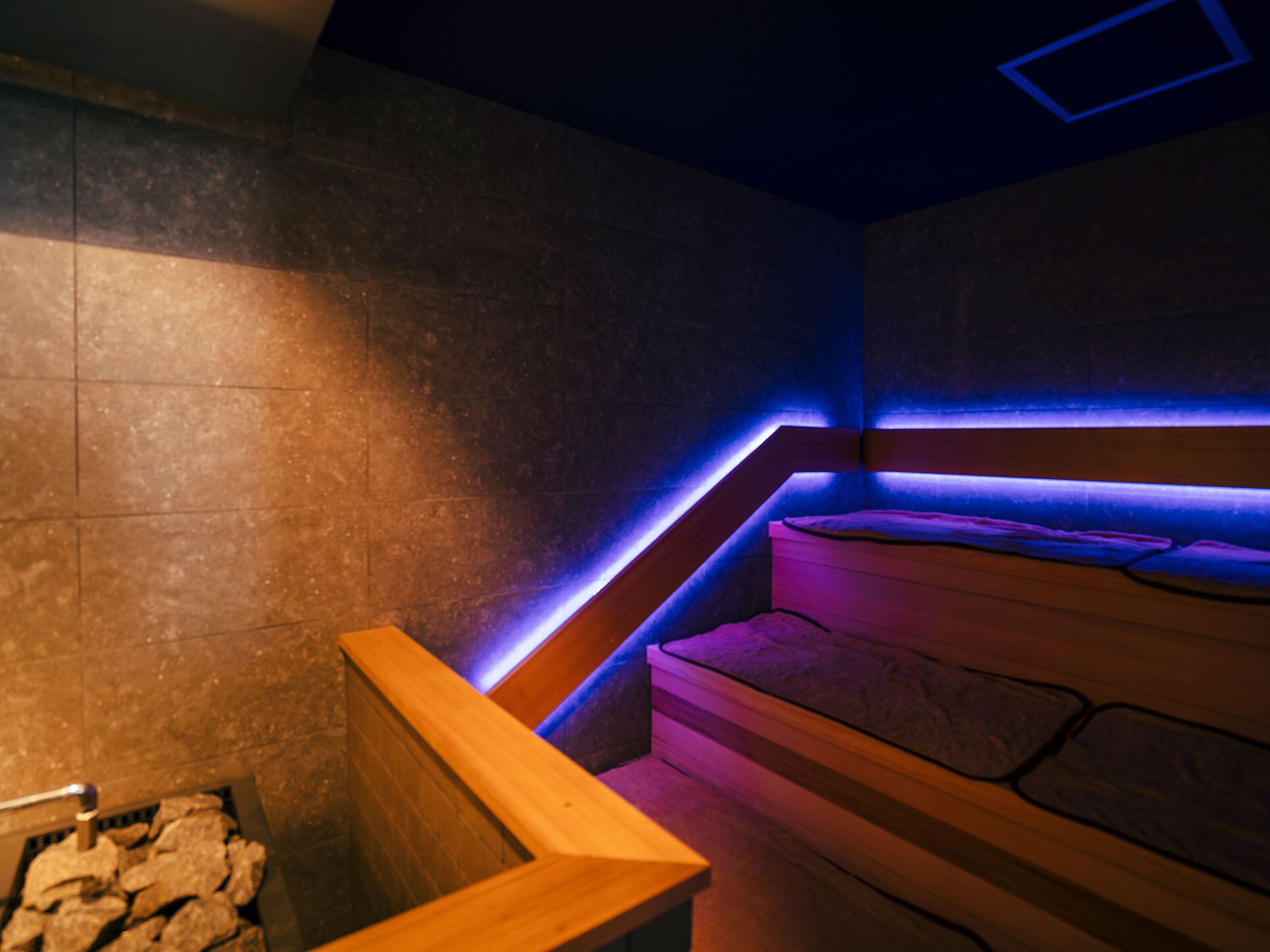 Un espace de bien-être moderne avec un banc en bois, des murs en pierre et un bord illuminé de lumière bleue.