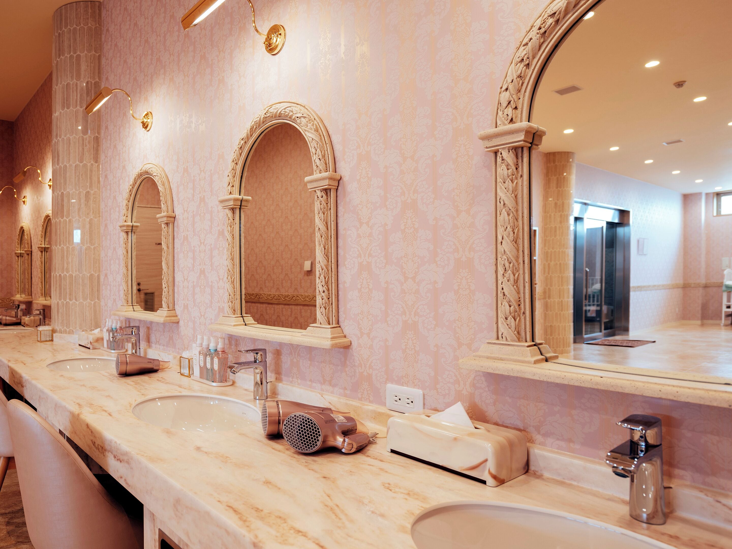 Een luxe badkamer met marmeren aanrechtbladen, meerdere wastafels en sierlijke spiegels.