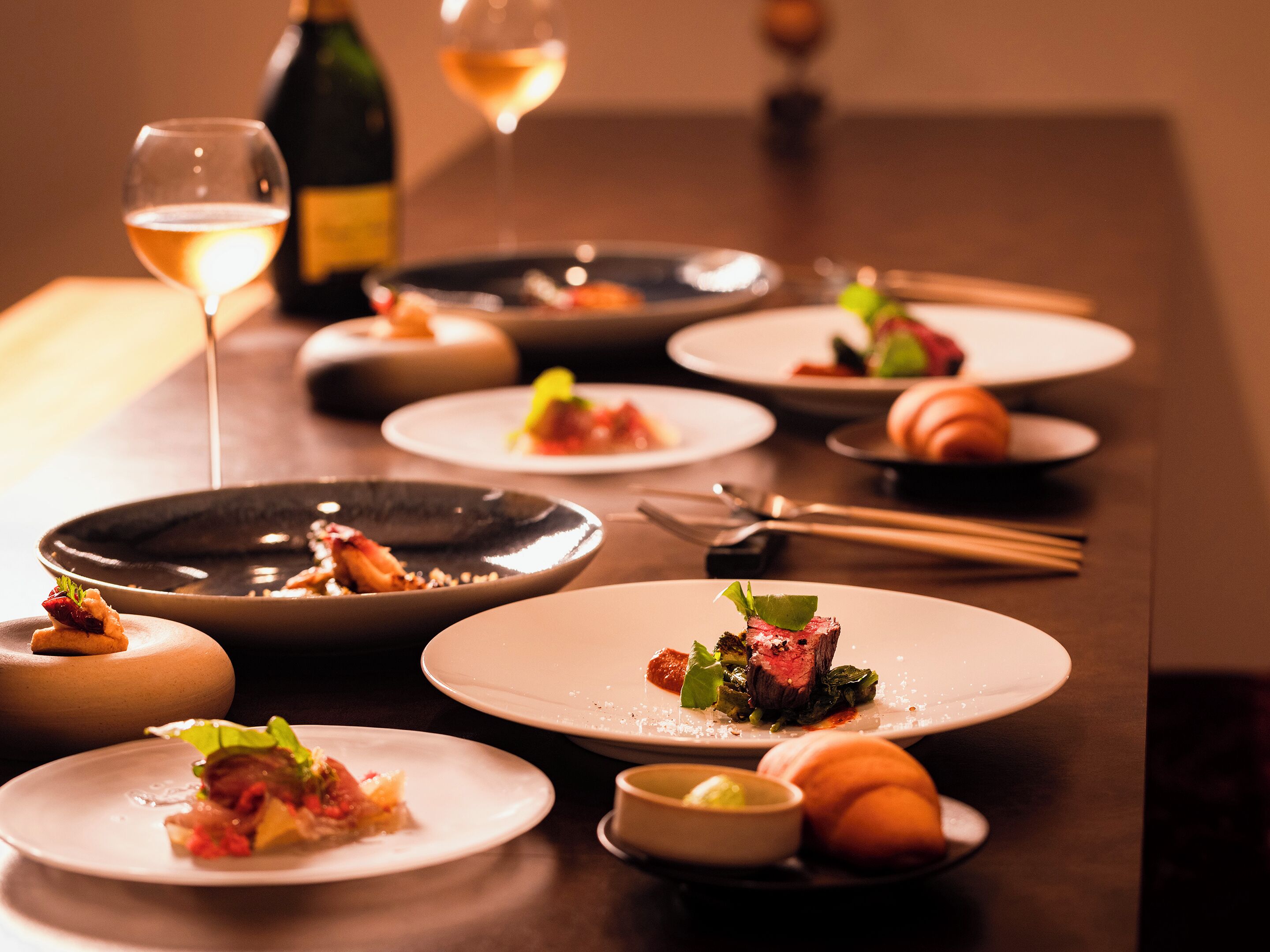 A dining table with multiple plates of food, a bottle of wine, and a glass of wine.