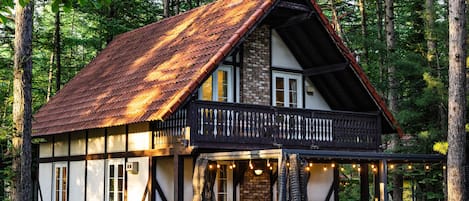 A traditional wooden house with a sloped roof, a balcony with a railing, and a stone chimney.