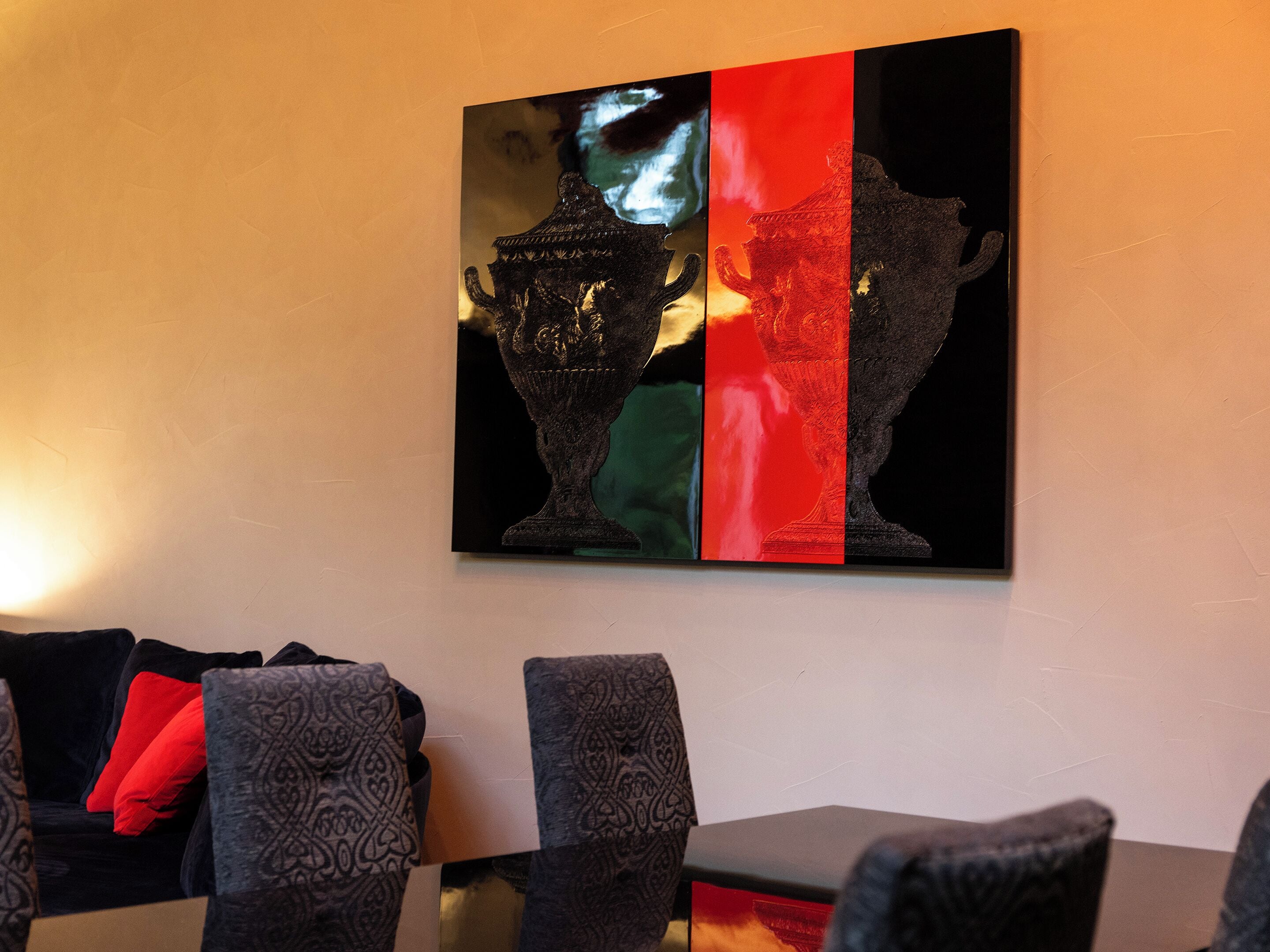 A dining area with a table and chairs, a wall-mounted artwork, and a sofa with patterned cushions.