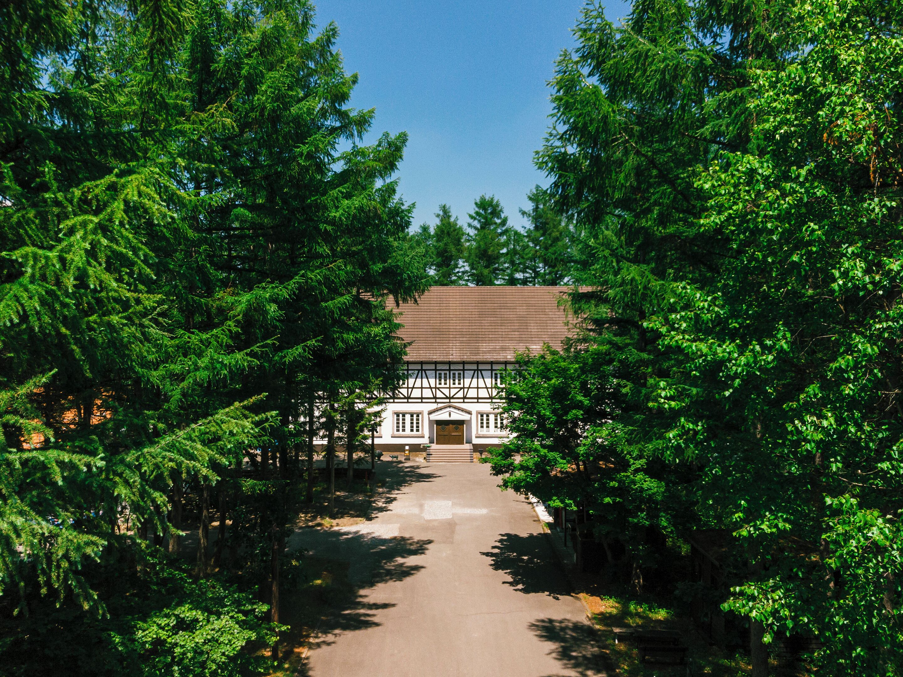 A traditional timber-framed building with a symmetrical facade, surrounded by dense evergreen trees.