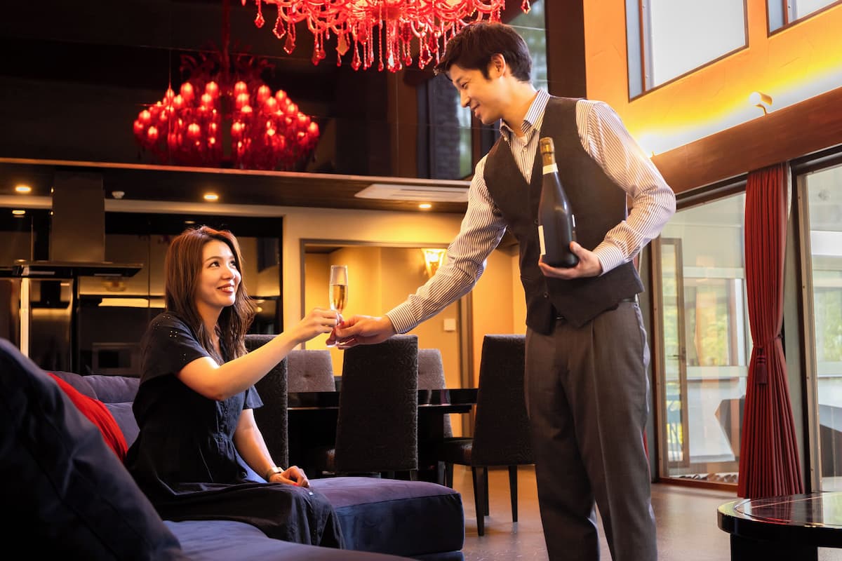 A man and a woman in a modern hotel lobby with a chandelier, seating area, and large windows.