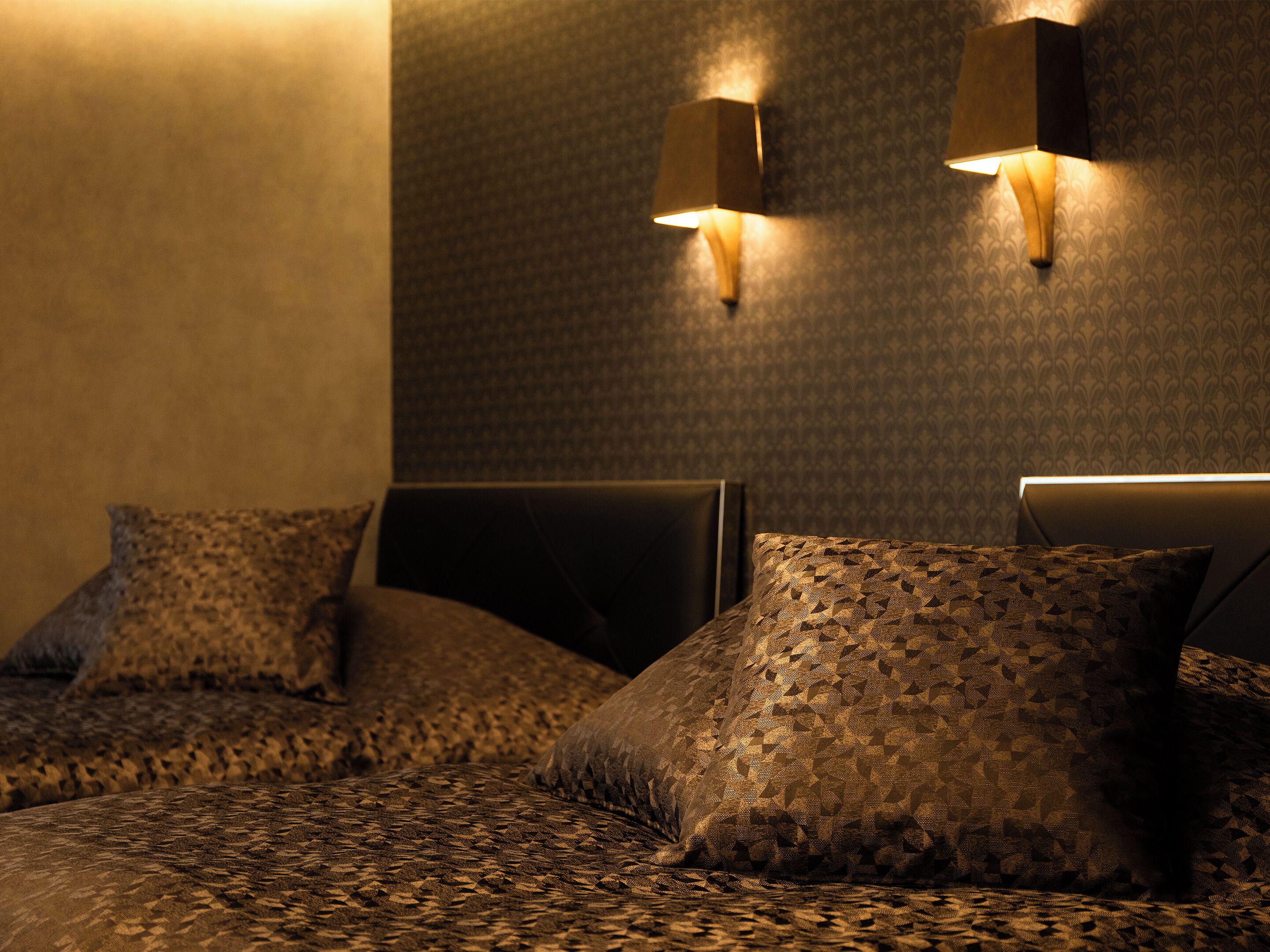 Habitación de hotel con una colcha estampada, dos lámparas fijadas a la pared y una pared con textura.
