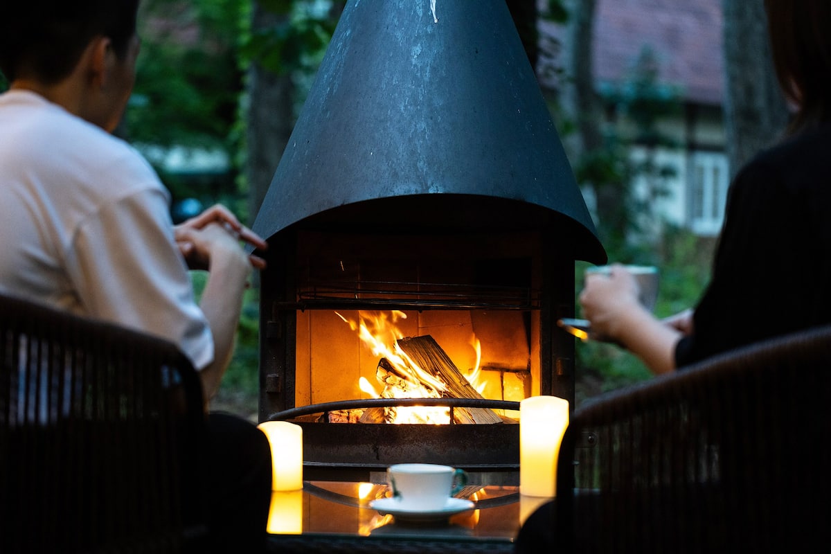A wood-fired oven with a conical roof, surrounded by chairs and a table with a cup and saucer.