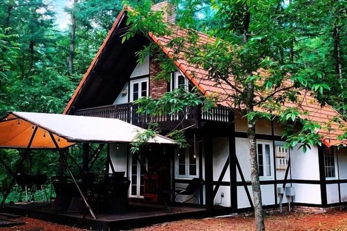 A traditional timber-framed house with a sloped roof, a porch, and a large umbrella.