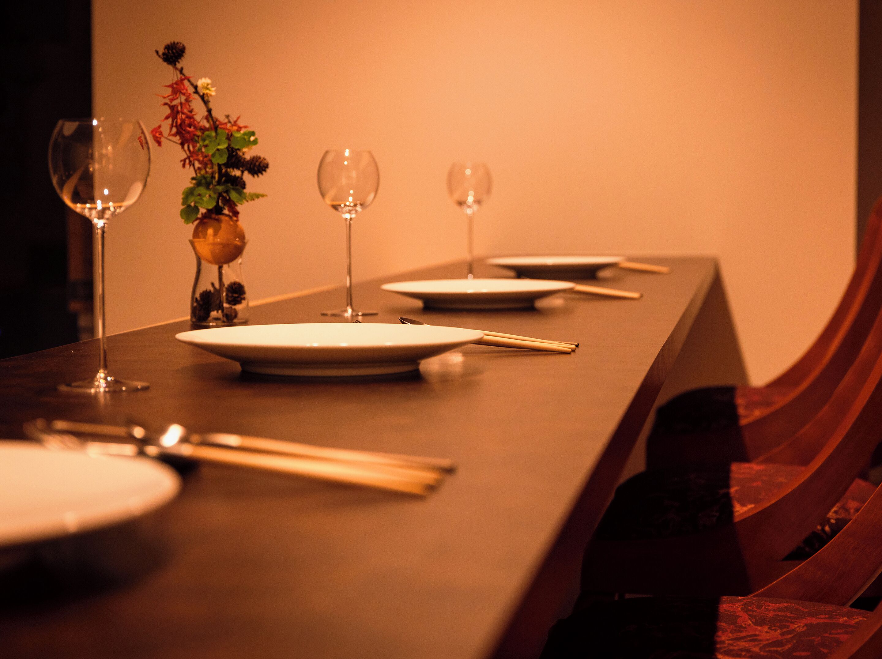 A long dining table with plates, cutlery, and wine glasses set for a meal.