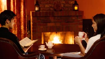 A cozy room with a brick fireplace, leather chairs, a table with a teapot and cups, and a person reading a book.