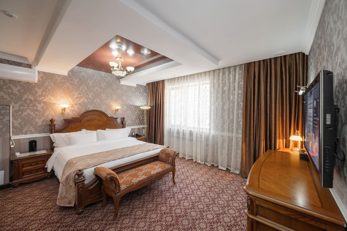 A hotel room with a large bed, a wooden bench, a TV, and a chandelier.