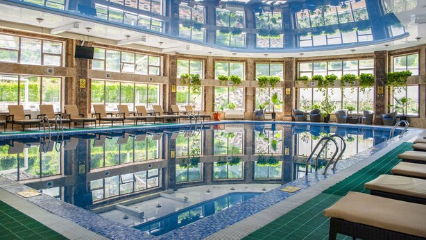 A large indoor swimming pool with multiple levels of seating and sunlit areas. - Jannat Resort (Koy-Tash)
