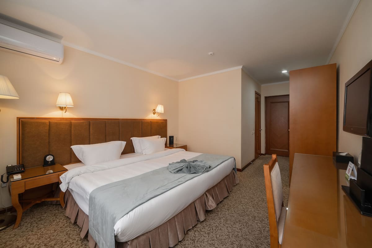 A hotel room with a large bed, bedside lamps, a desk with a telephone, and a television.