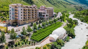 A multi-story hotel with balconies, surrounded by lush greenery and a river. - Jannat Resort (Koy-Tash)