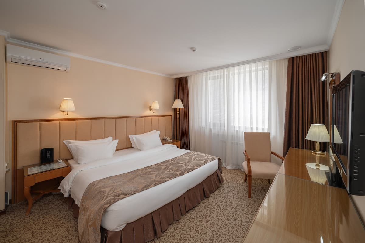 A hotel room with a large bed, a desk with a chair, a television, and a window with curtains.